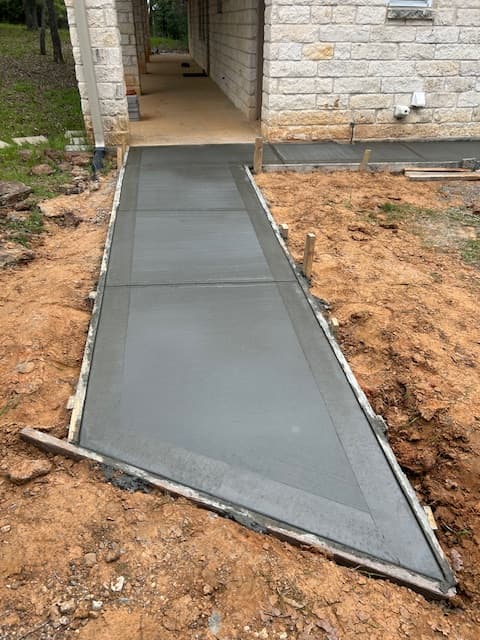 Smooth grey concrete walkway with sharp angled edge under construction next to stone building.