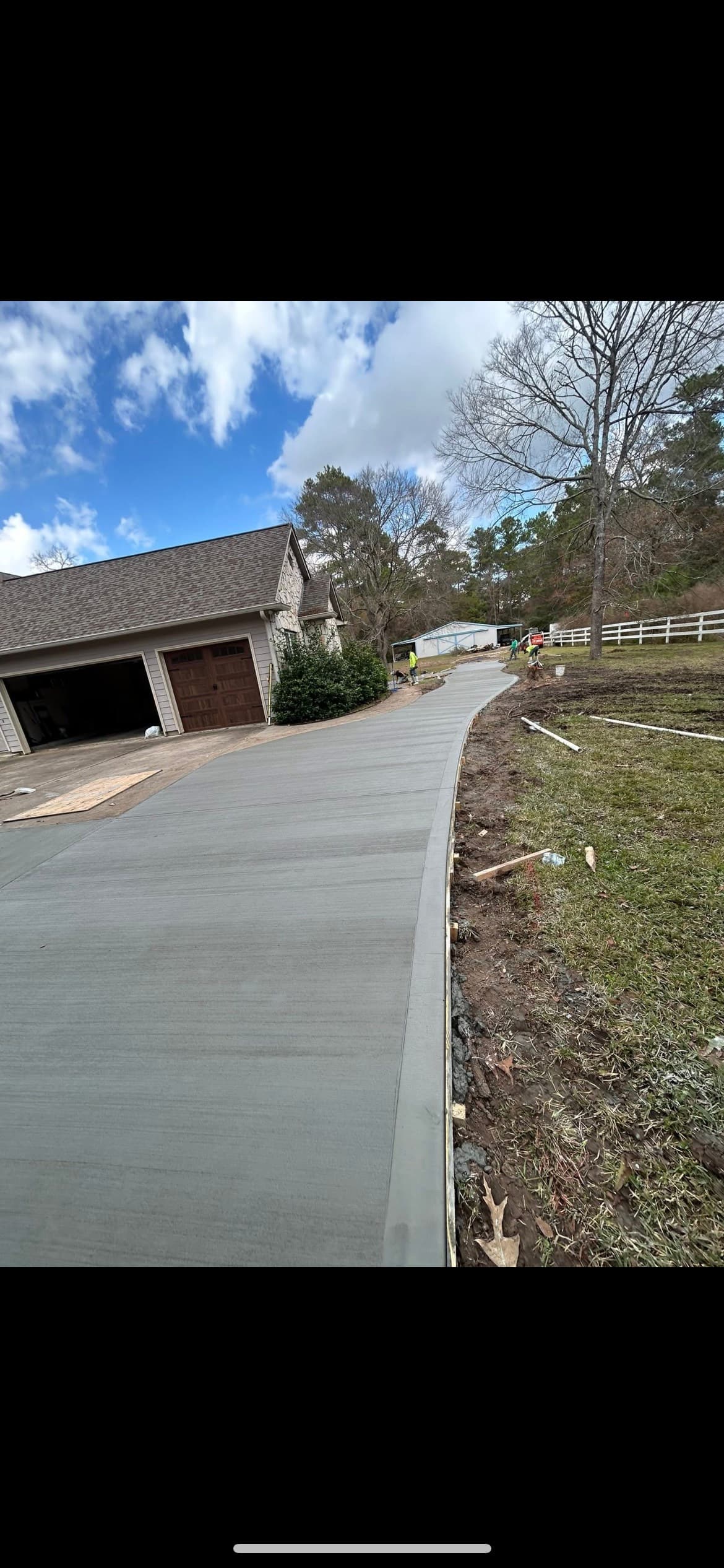 Newly poured, curved concrete driveway with a brushed finish leading away from a residential garage.